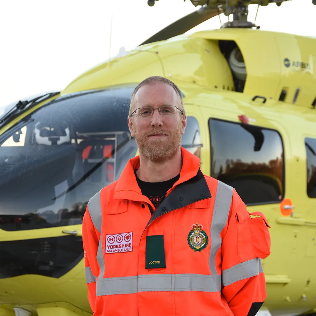 Yorkshire Air Ambulance Doctor Neil Sambridge stood in front of a yellow YAA helicopter