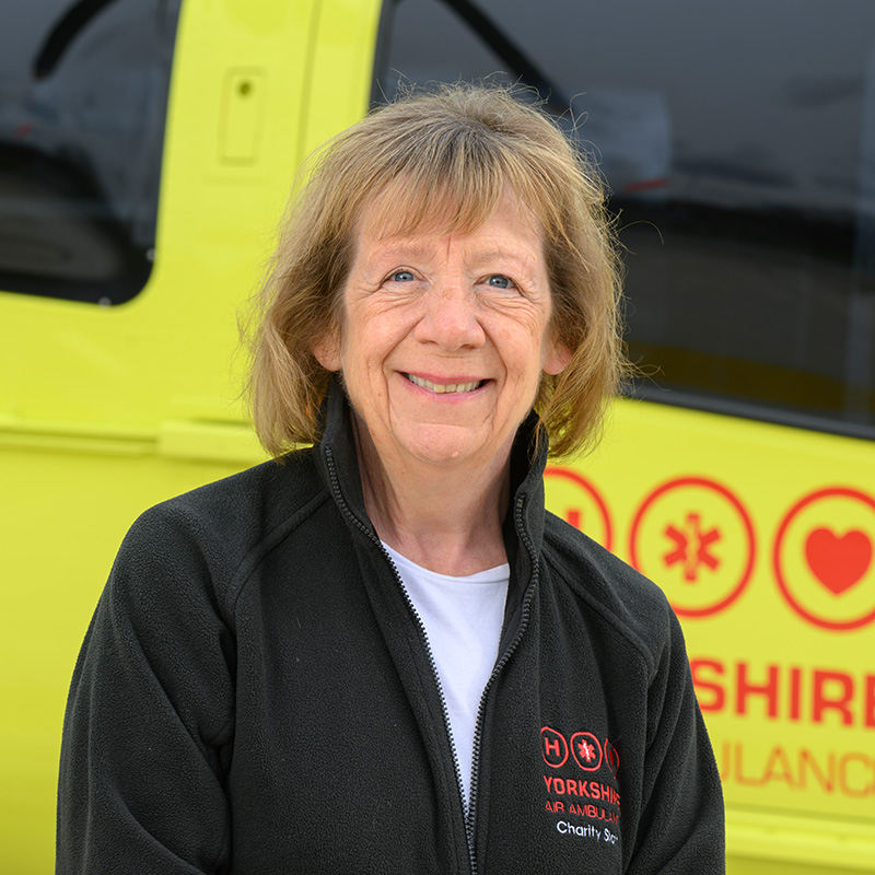 A woman wearing a black fleece and white top is standing in front of a yellow helicopter