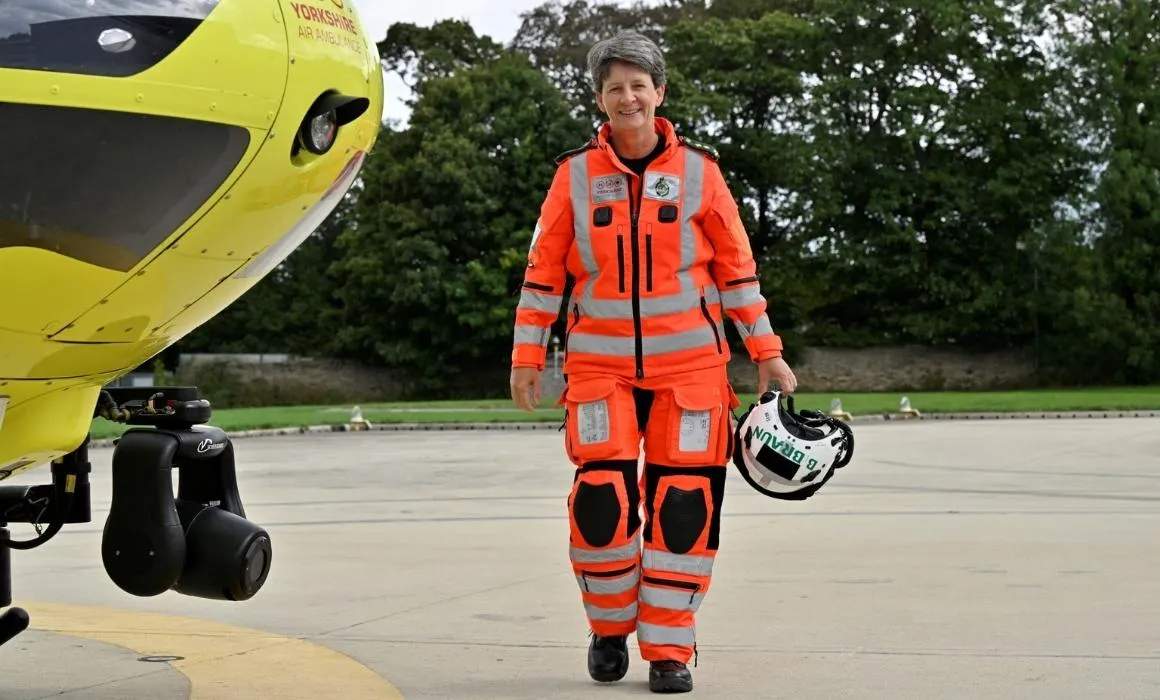 Yorkshire Air Ambulance HEMS Paramedic Sammy Wills walks past one of the yellow Yorkshire Air Ambulance helicopters, wearing her bright orange flying suit and carrying her white helmet