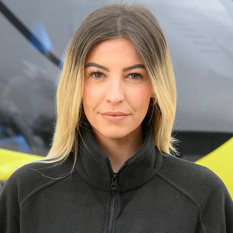 Woman wearing a black fleece standing in front of a yellow helictoper