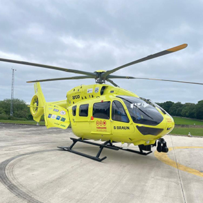 A yellow five-bladed helicopter stands on a helipad.