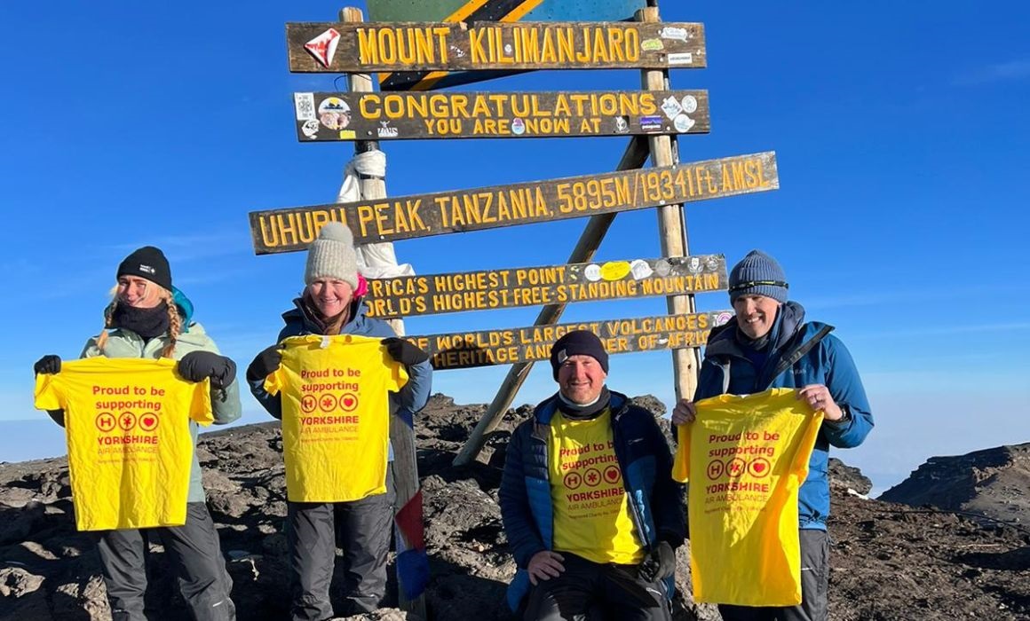 four people in front of a sign holding Yorkshire Air Ambulance T-shirts